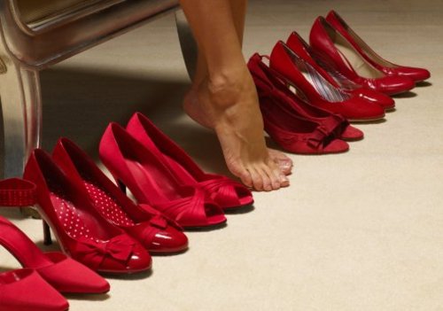 Woman's bare feet amongst row of red shoes, close-up